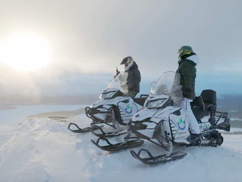 Zwei vollelektrische Schneemobile mit Fahrern auf einem Hügel in Schnee in Finnland